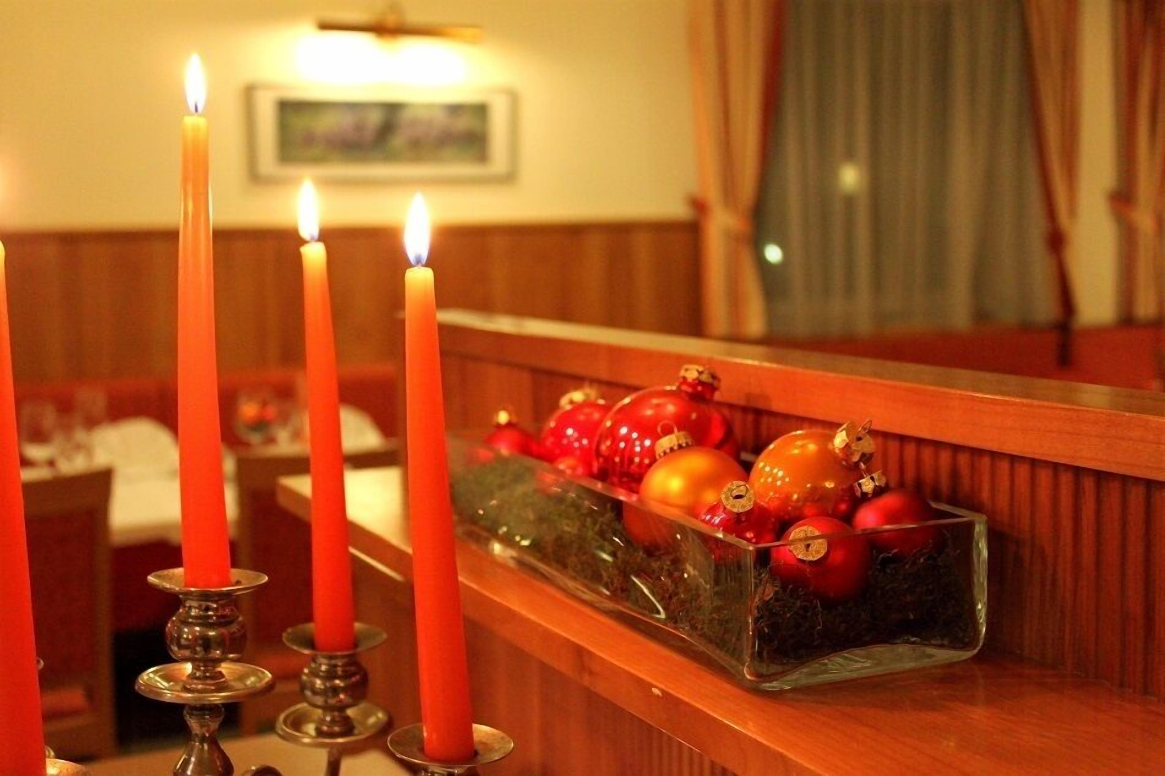 Ein Kerzenlicht beleuchtet einen Tisch mit einem Glasgefäß, das rote und goldene Weihnachtsdekorationen enthält.
