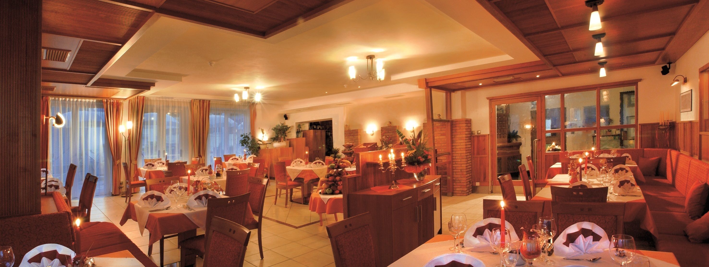 A dining area with multiple tables set for meals, wooden ceiling beams, and a brick fireplace.