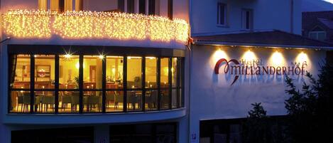A building with a restaurant named "Hotel Andererhof" featuring large windows and a balcony with string lights.