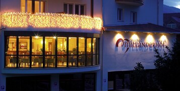 Un edificio con restaurante llamado "Hotel Andererhof", con grandes ventanales y un balcón adornado con luces de cuerda.