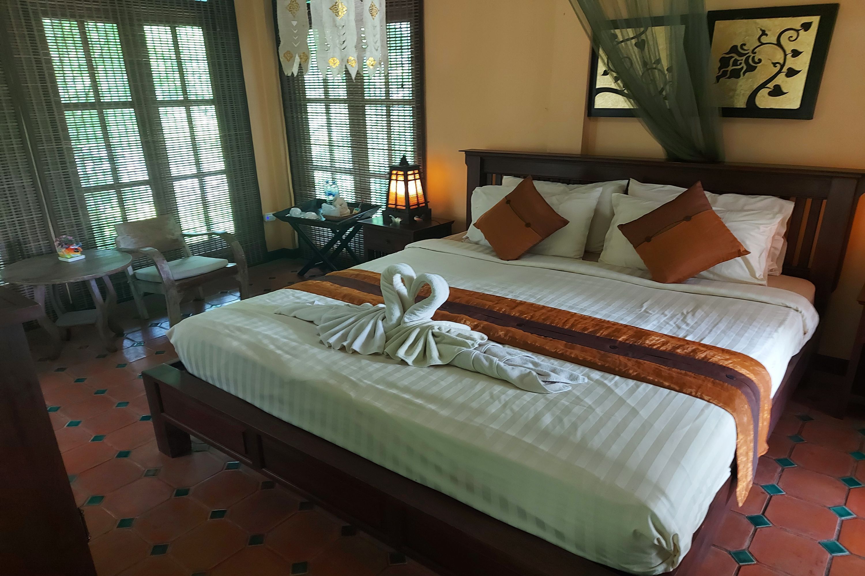 A neatly made bed with a towel swan, a bedside table with a lamp, and a chair.