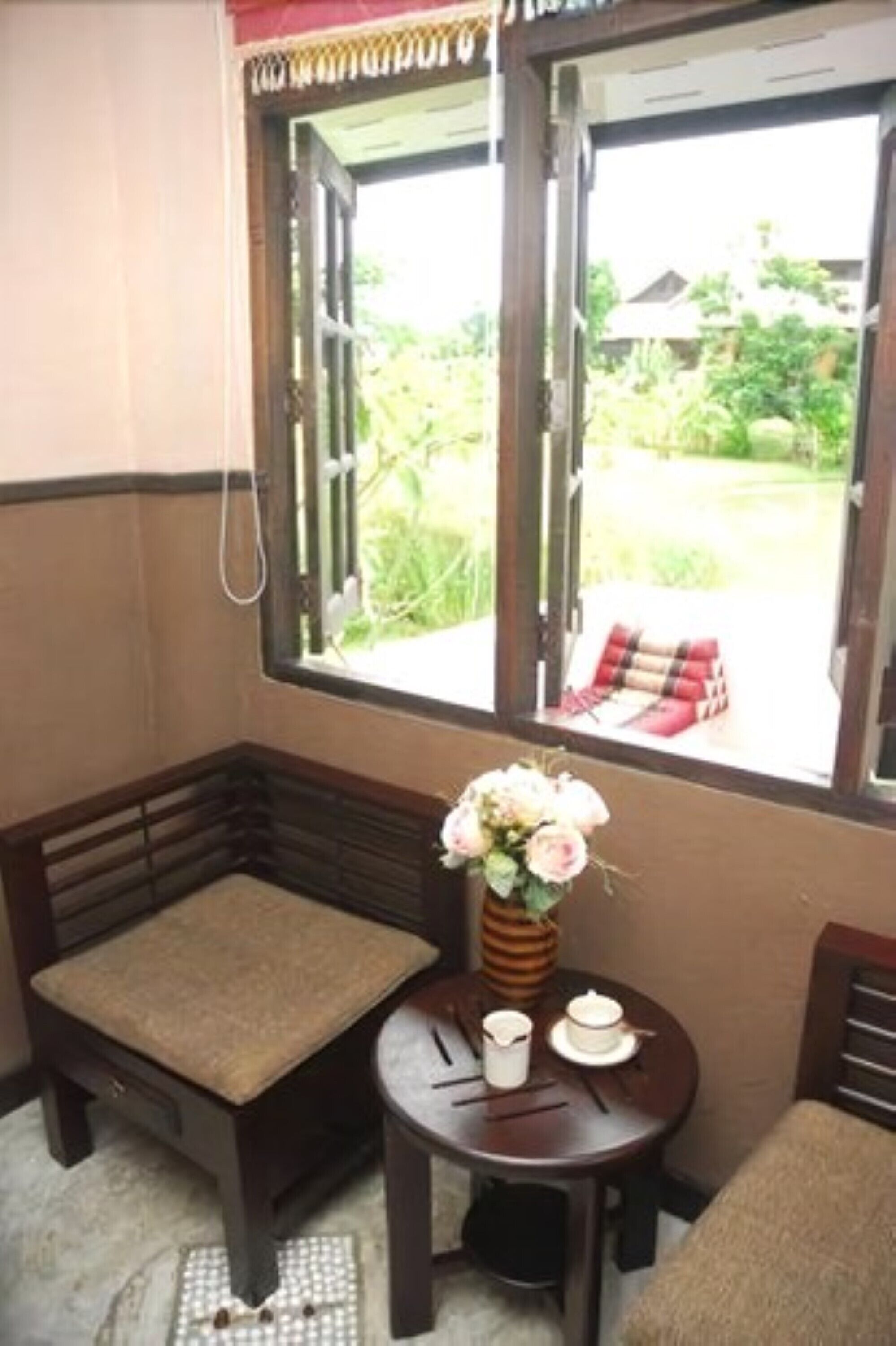 A small room with a wooden bench, a small table with a vase of flowers, and a window with a view of greenery outside.