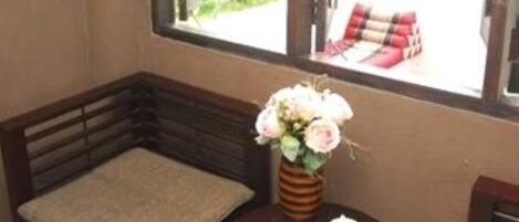 A small room with a wooden bench, a small table with a vase of flowers, and a window with a view of greenery outside.