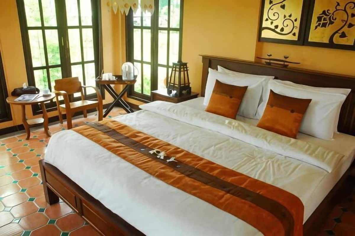 Una cama bien tendida con una colcha a rayas, una mesita de noche de madera con una lámpara, y una silla.