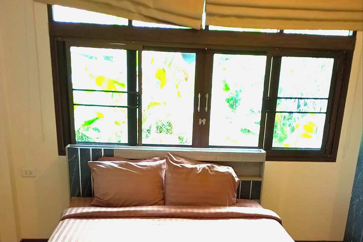 Una cama bien hecha con una colcha marrón y almohadas, un cabecero de madera y una ventana con vistas a la vegetación.