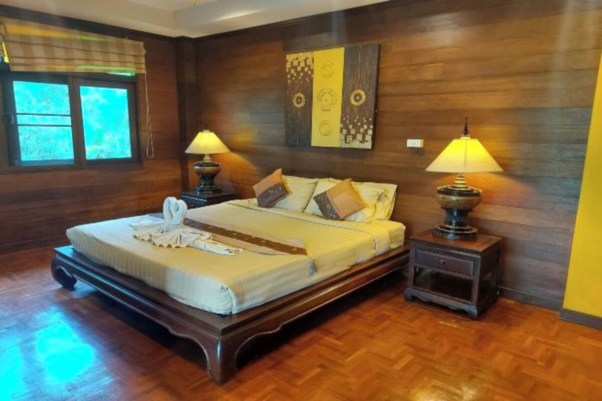 Una cama bien hecha con toalla, dos lámparas de noche y un cabecero de madera.