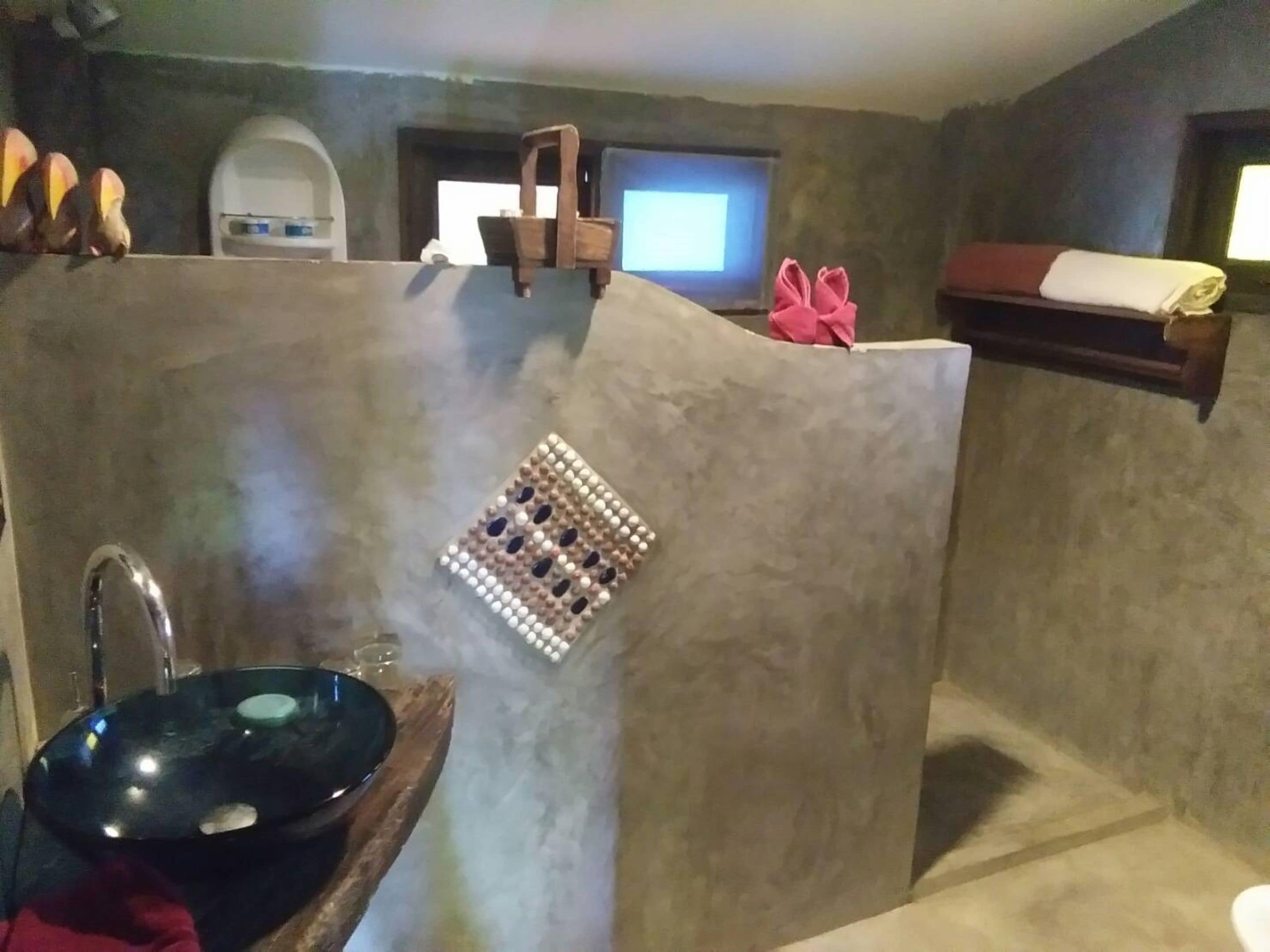 A bathroom with a stone sink, a shower area, and a wooden chair.
