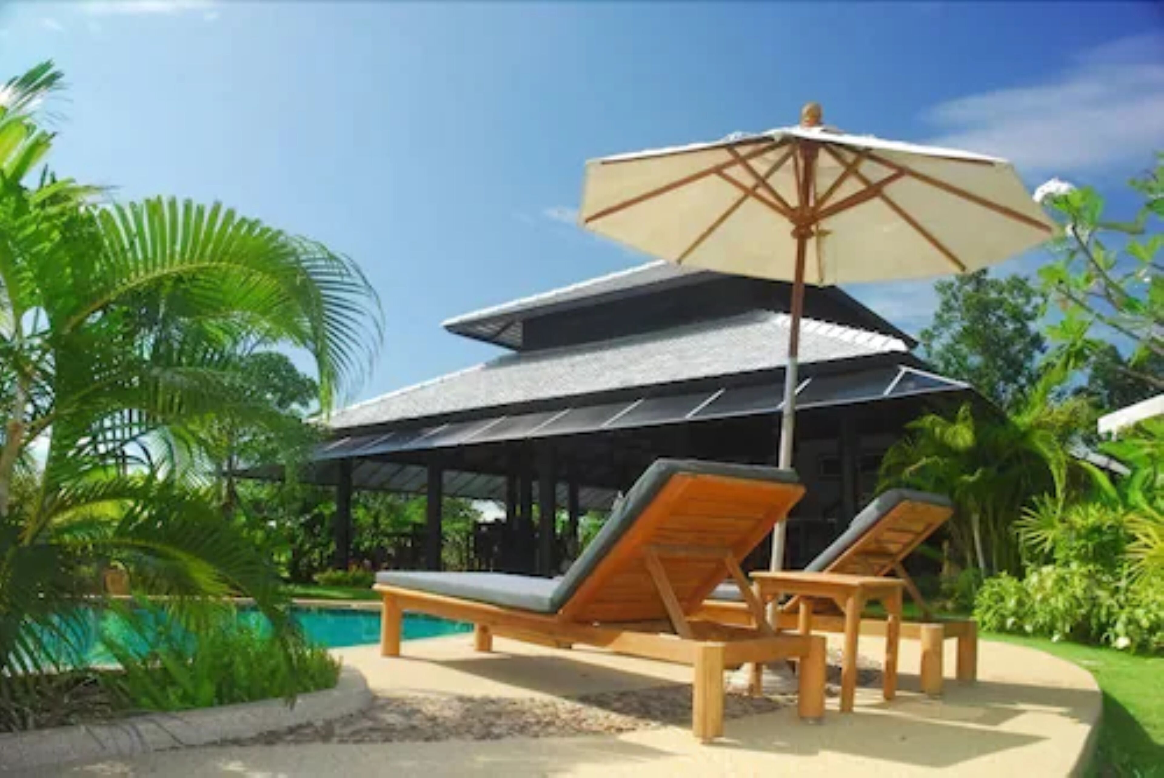 Un espace aménagé au bord de la piscine, avec des chaises longues et un parasol, le tout entouré d’une végétation luxuriante.