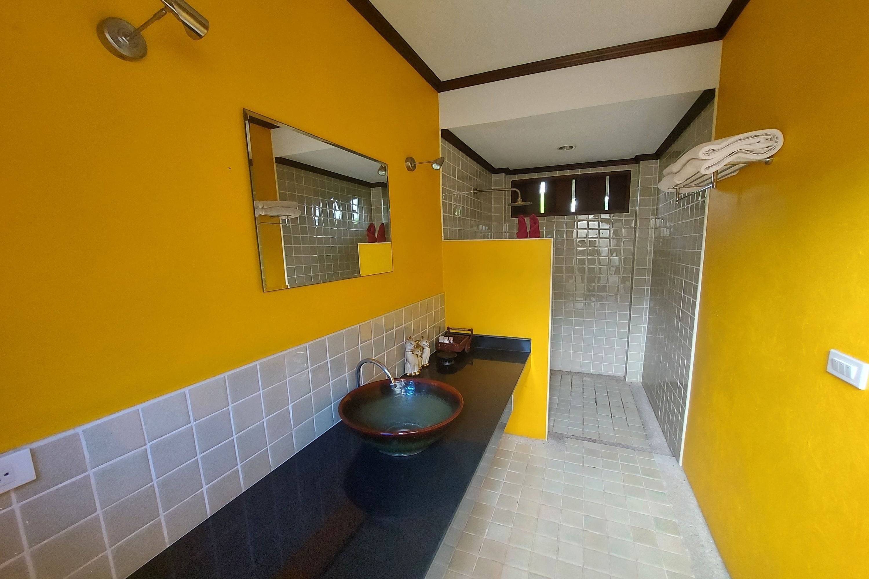 A bathroom with a yellow wall, a black sink, a mirror, and a shower area.