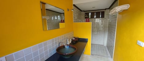 A bathroom with a yellow wall, a black sink, a mirror, and a shower area.