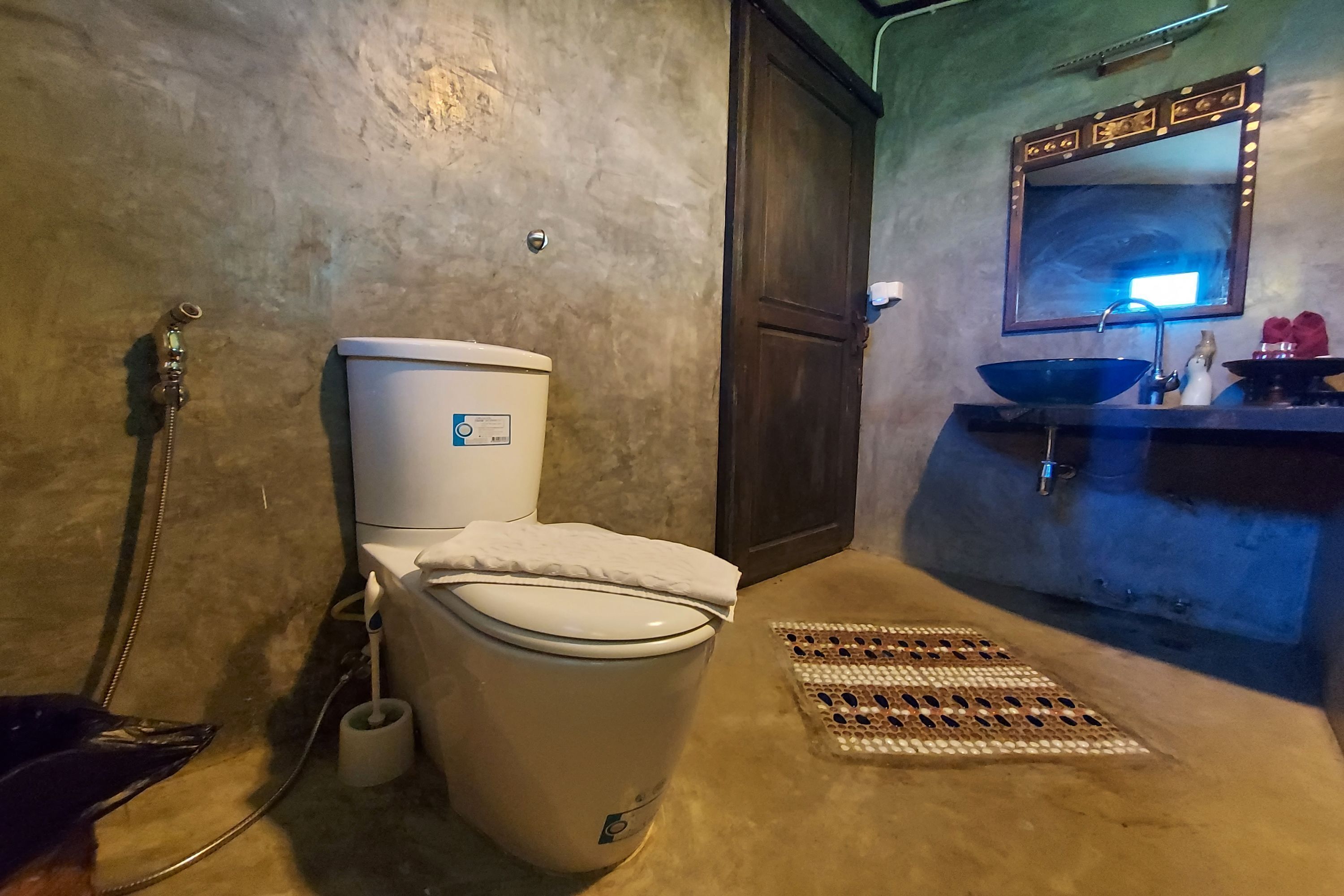 Un baño con inodoro, bidé, lavabo con espejo y un felpudo estampado en el suelo.