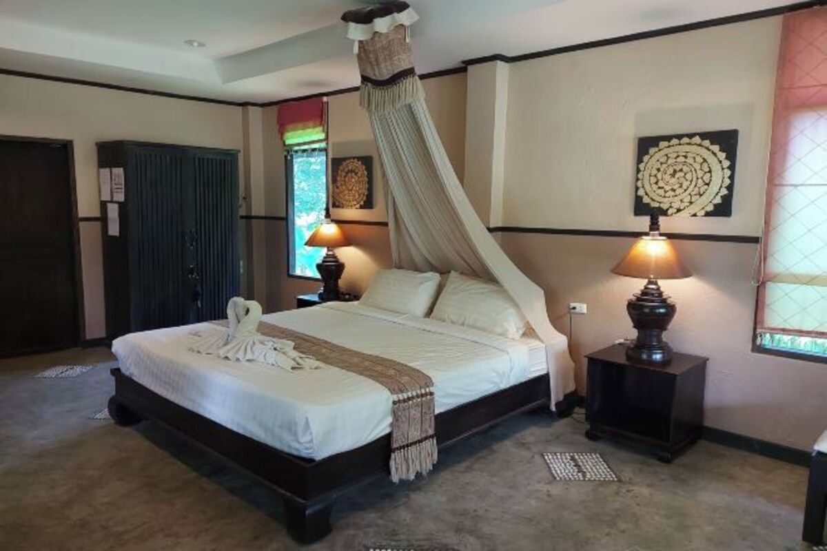 Un dormitorio con cama con dosel, dos lámparas de noche, un adorno en la pared y una ventana con cortinas.