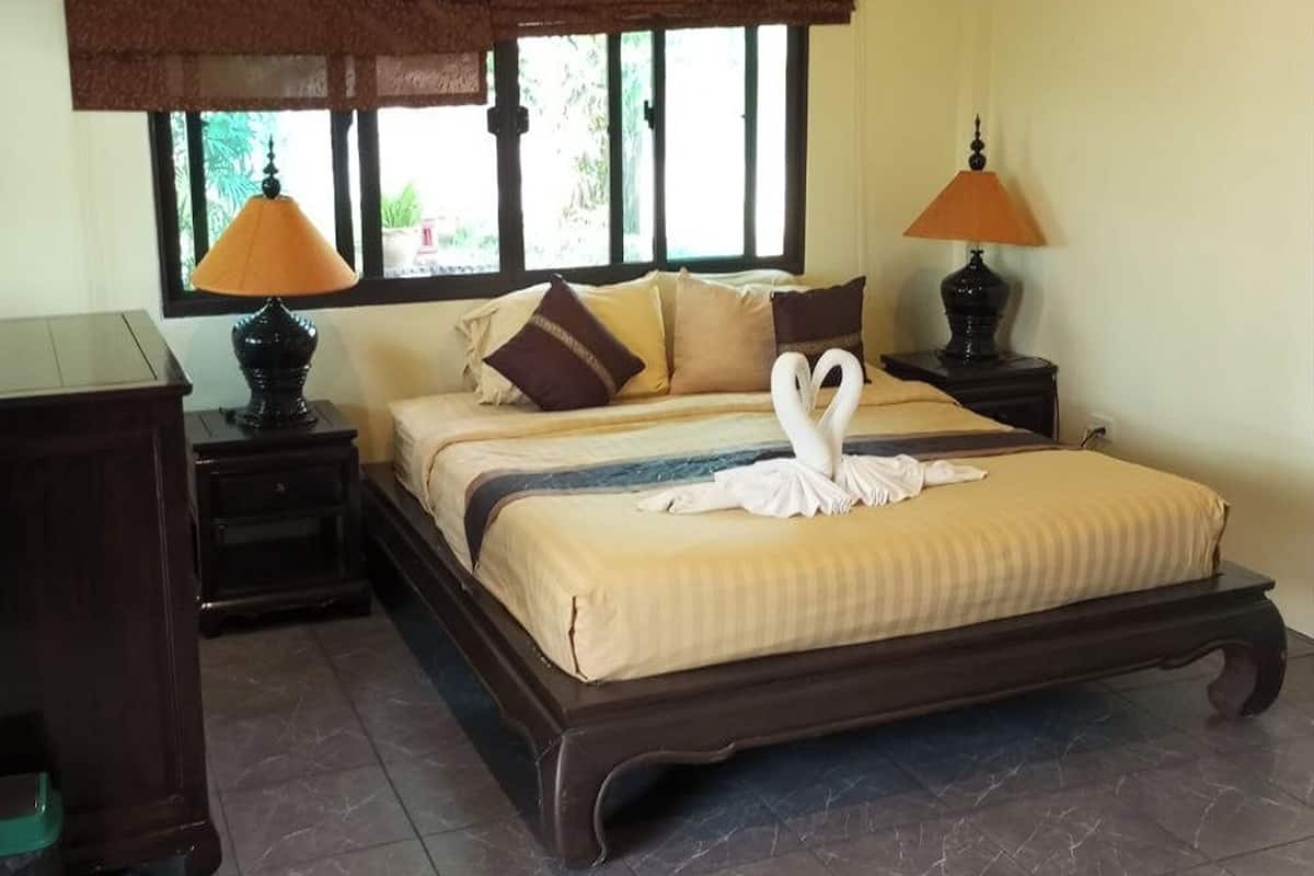 Habitación de hotel con cama, dos mesitas de noche, lámparas, una ventana con cortinilla marrón y decoración de cisne en la cama.