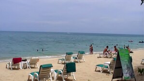 A beach with rows of sun loungers and a signboard. - Utopia Resort (Koh Samui)