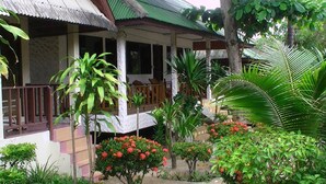 A traditional house with a porch, surrounded by lush greenery and flowering plants. - Utopia Resort (Koh Samui)