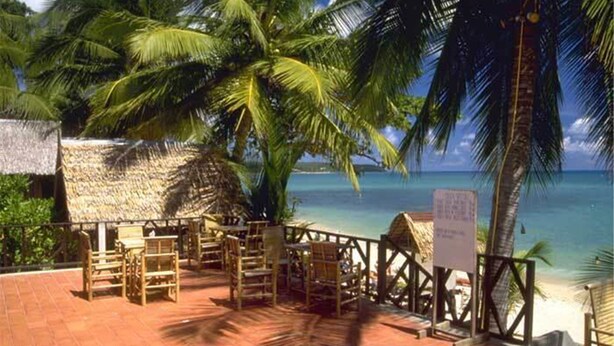 A beachside restaurant with thatched-roof tables and chairs, overlooking the ocean. - Utopia Resort (Koh Samui)