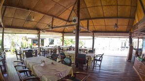 An open-air restaurant with wooden tables and chairs, a thatched roof, and a view of the sea. - Utopia Resort (Koh Samui)