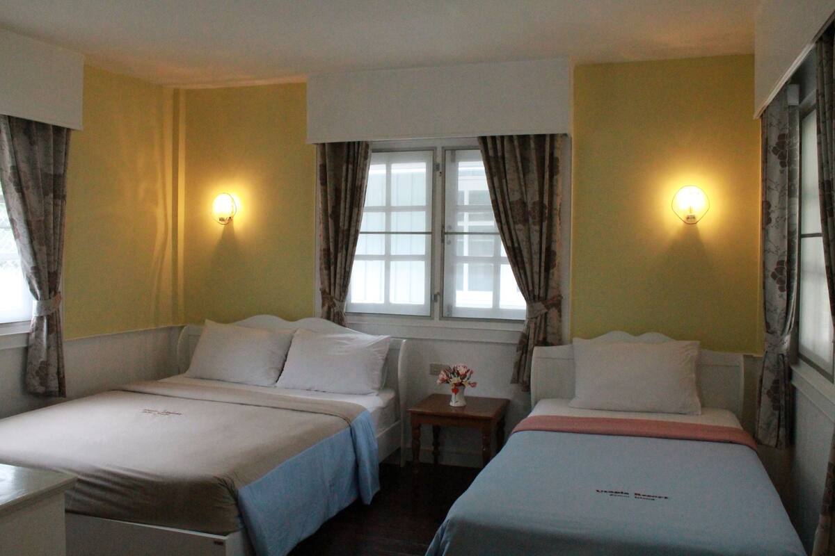 A hotel room with two single beds, a small table with a vase, and two wall-mounted lights.