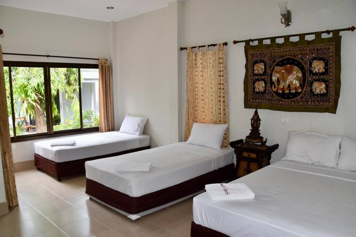 A hotel room with two single beds, a large window with curtains, and a decorative tapestry on the wall.