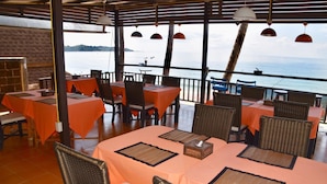 An outdoor dining area with tables and chairs, a view of the sea, and a covered section with hanging lights. - Magic Resort (Koh Samui)
