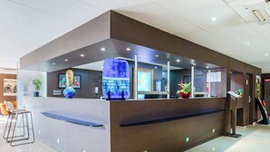 Ein moderner Empfangstresen mit Holzoptik, eine blaue Dekorationsvase und ein Bildschirm.