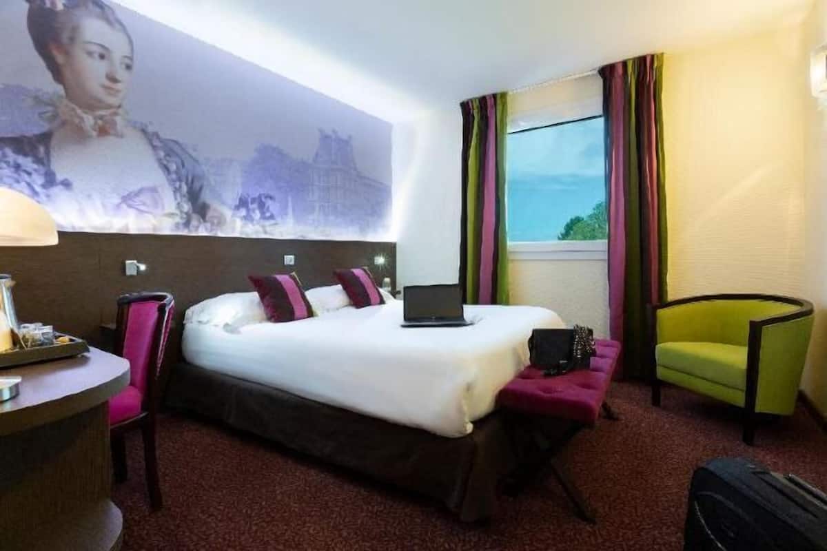 Ein Hotelzimmer mit Bett, Schreibtisch, Stuhl, Laptop und einem Fenster mit Vorhängen.