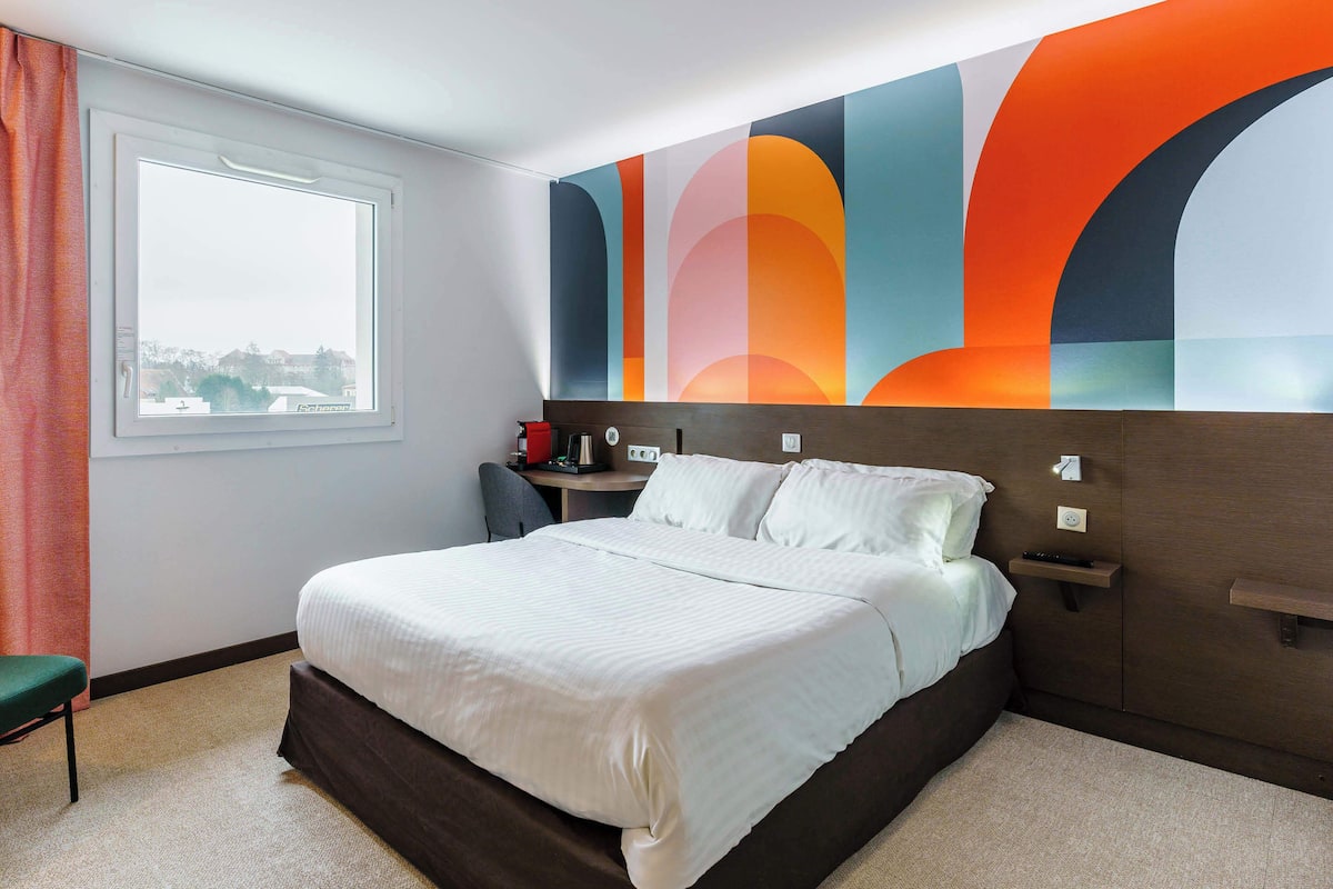 Ein modernes Hotelzimmer mit einem großen Bett, einem Schreibtisch und Blick auf die Stadt.