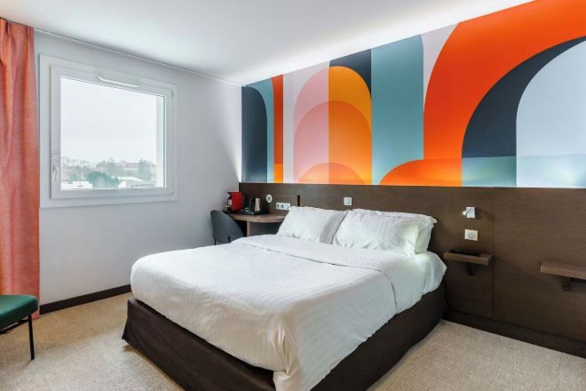 A hotel room with a large bed, a desk, a chair, and a window with curtains.