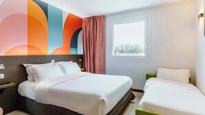 Ein Hotelzimmer mit einem großen Bett, einem kleineren Bett, einem Fenster und einem farbenfrohen Wandbild.