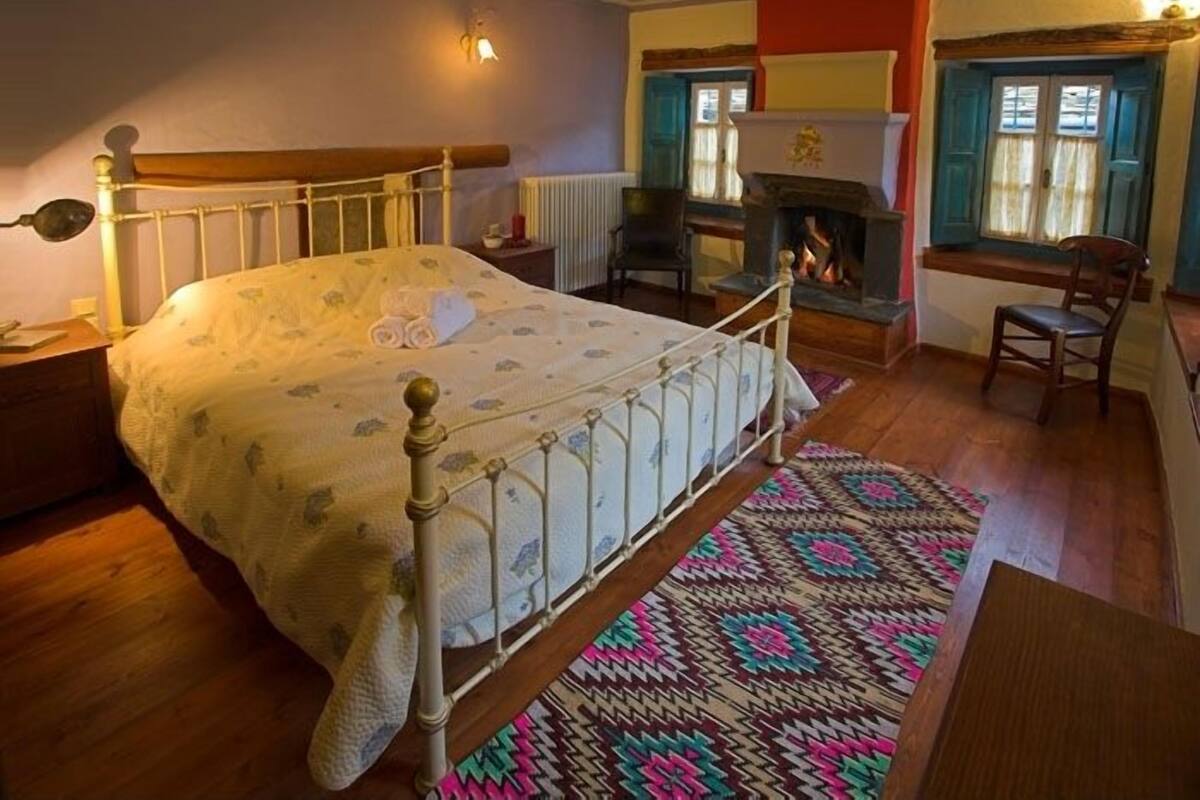 A traditional bedroom with a wooden bed, a fireplace, a patterned rug, and a window with curtains.