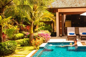 Une piscine entourée d’un jardin tropical, avec des chaises longues et un espace salon abrité.
