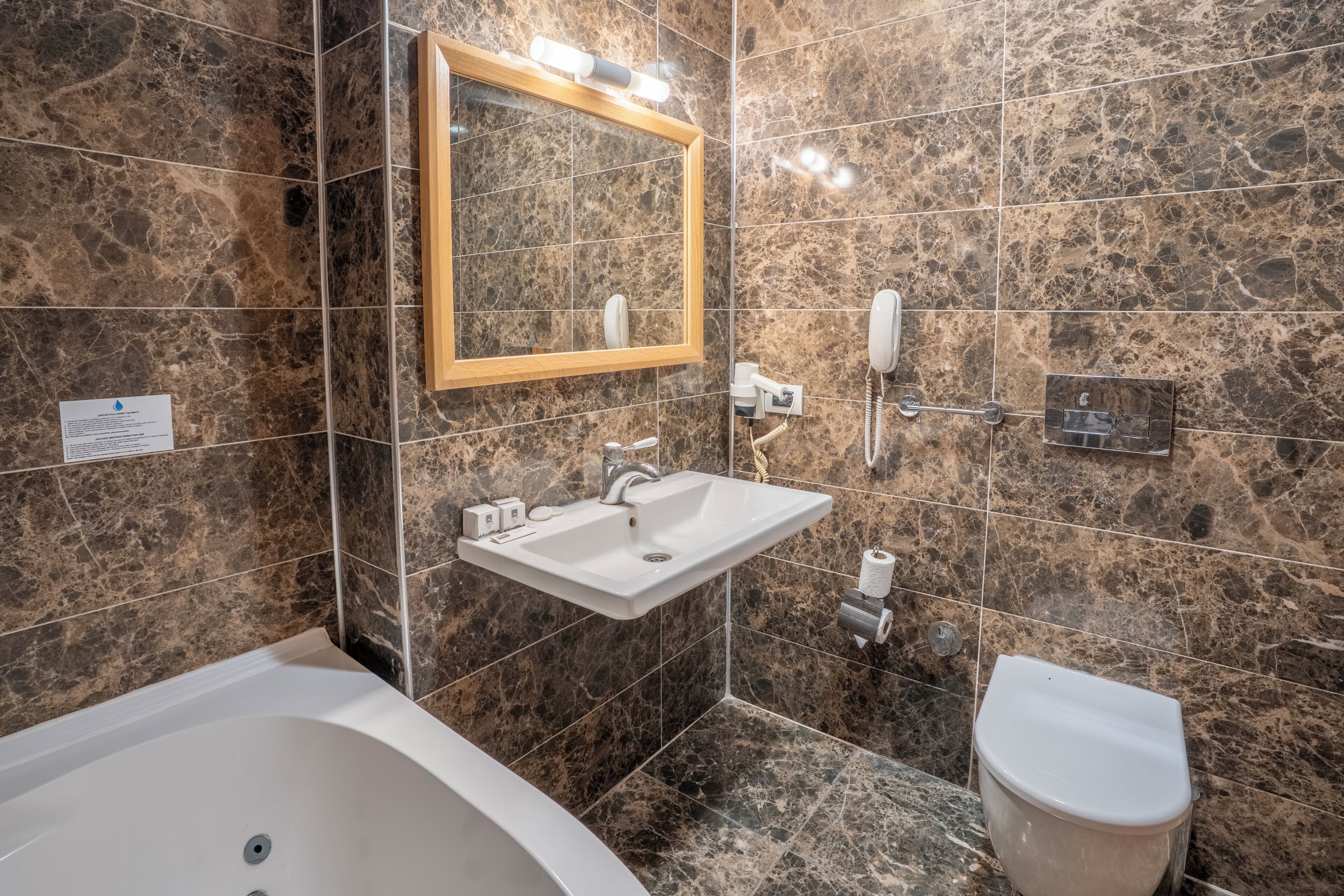 A bathroom with a marble wall, a white sink, a mirror, a toilet, and a bathtub.