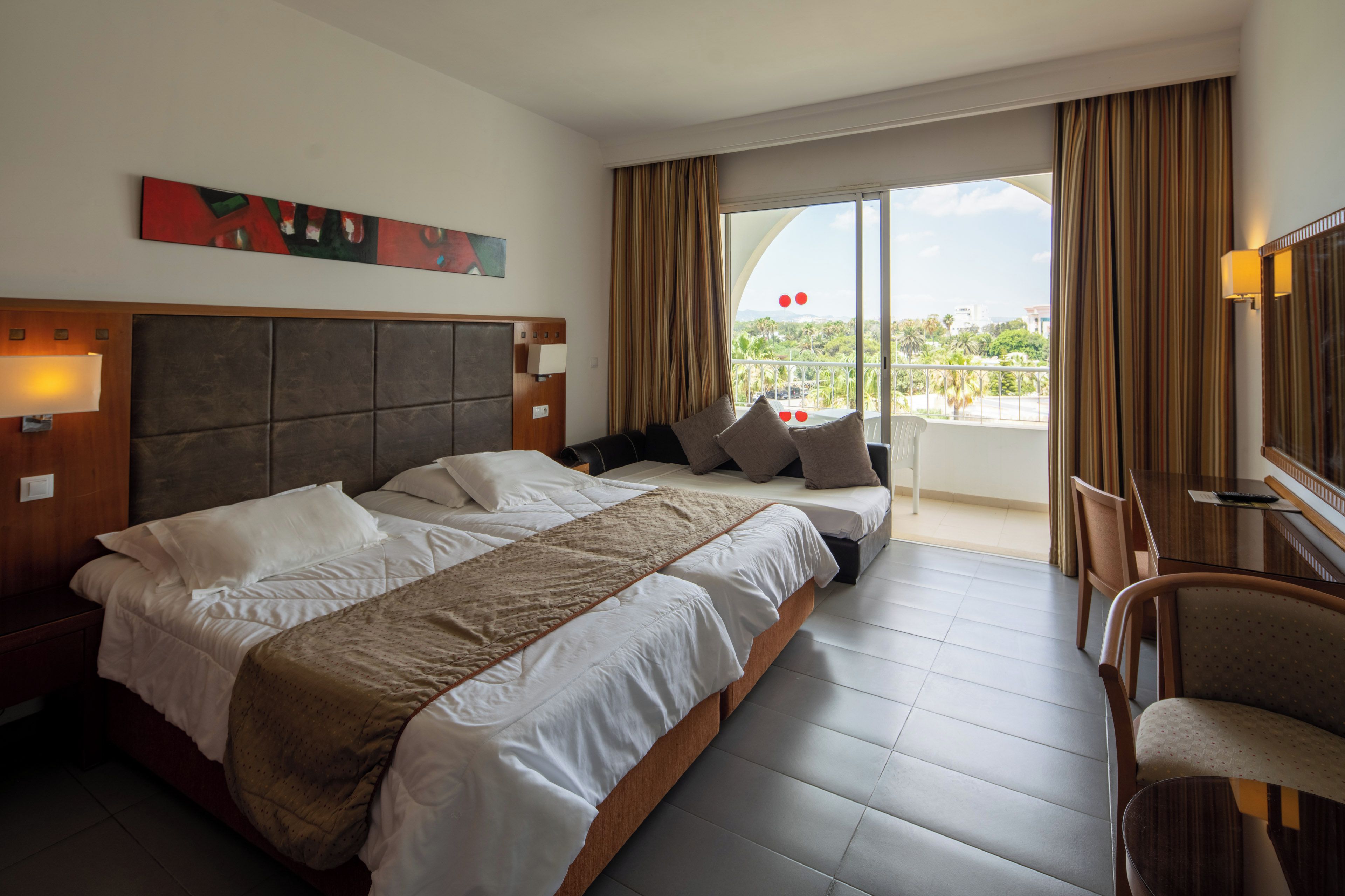 Habitación de hotel con una cama grande, un sofá, un escritorio y un balcón con vistas.