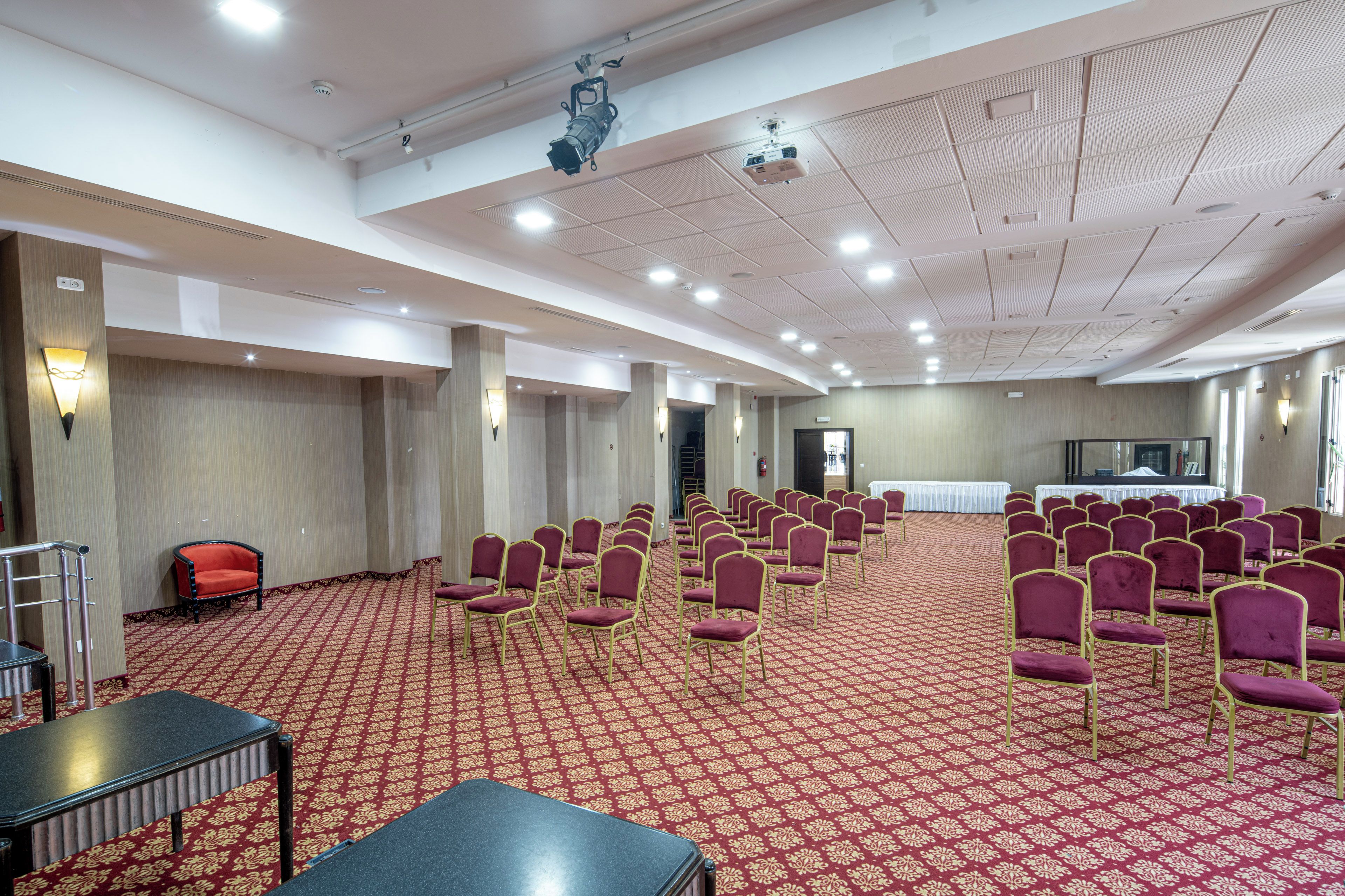 A conference room with rows of chairs, a stage, and a carpeted floor.