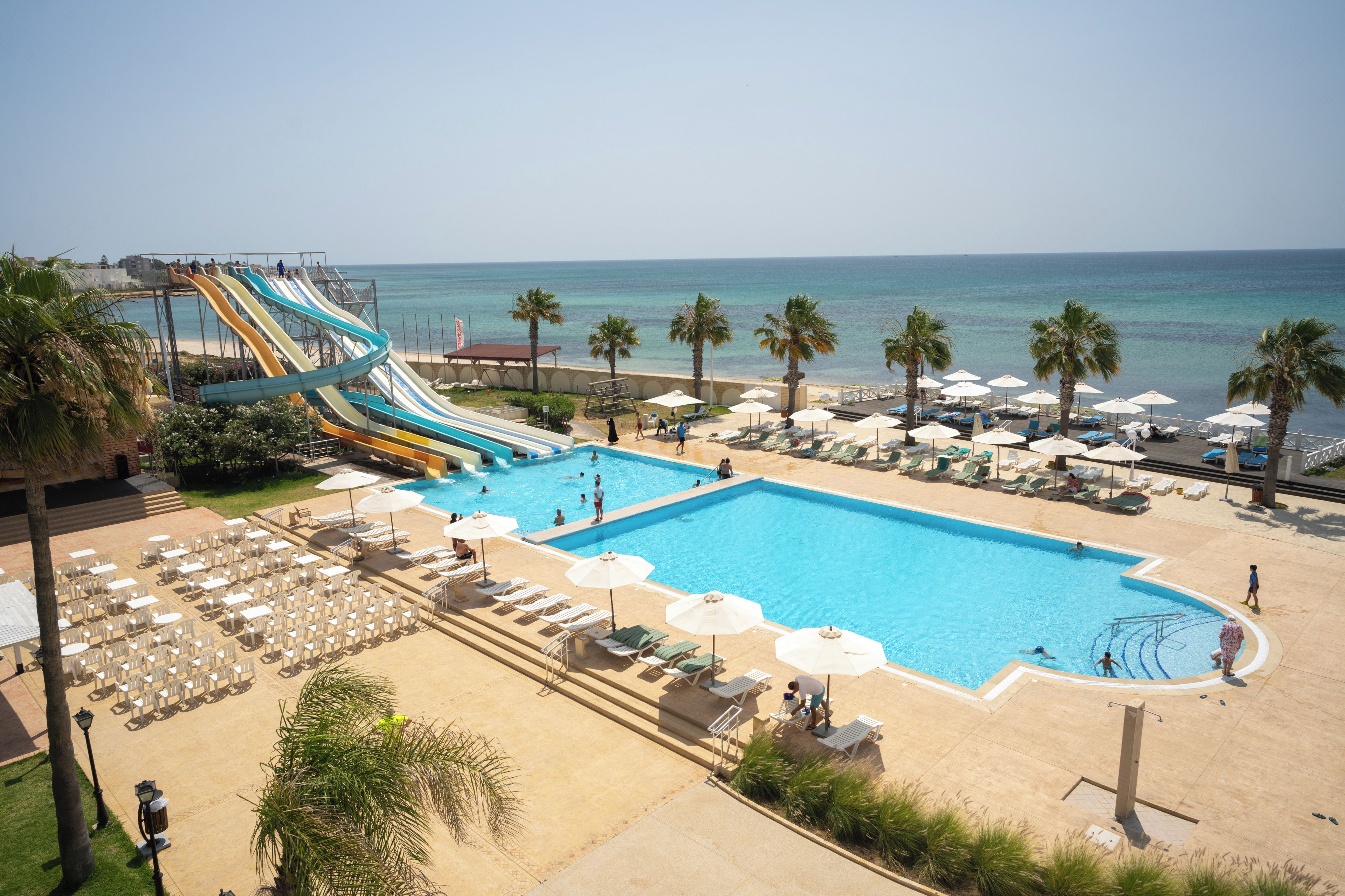 Un espace piscine doté d’un toboggan, de chaises longues, de parasols et offrant une vue sur l’océan.