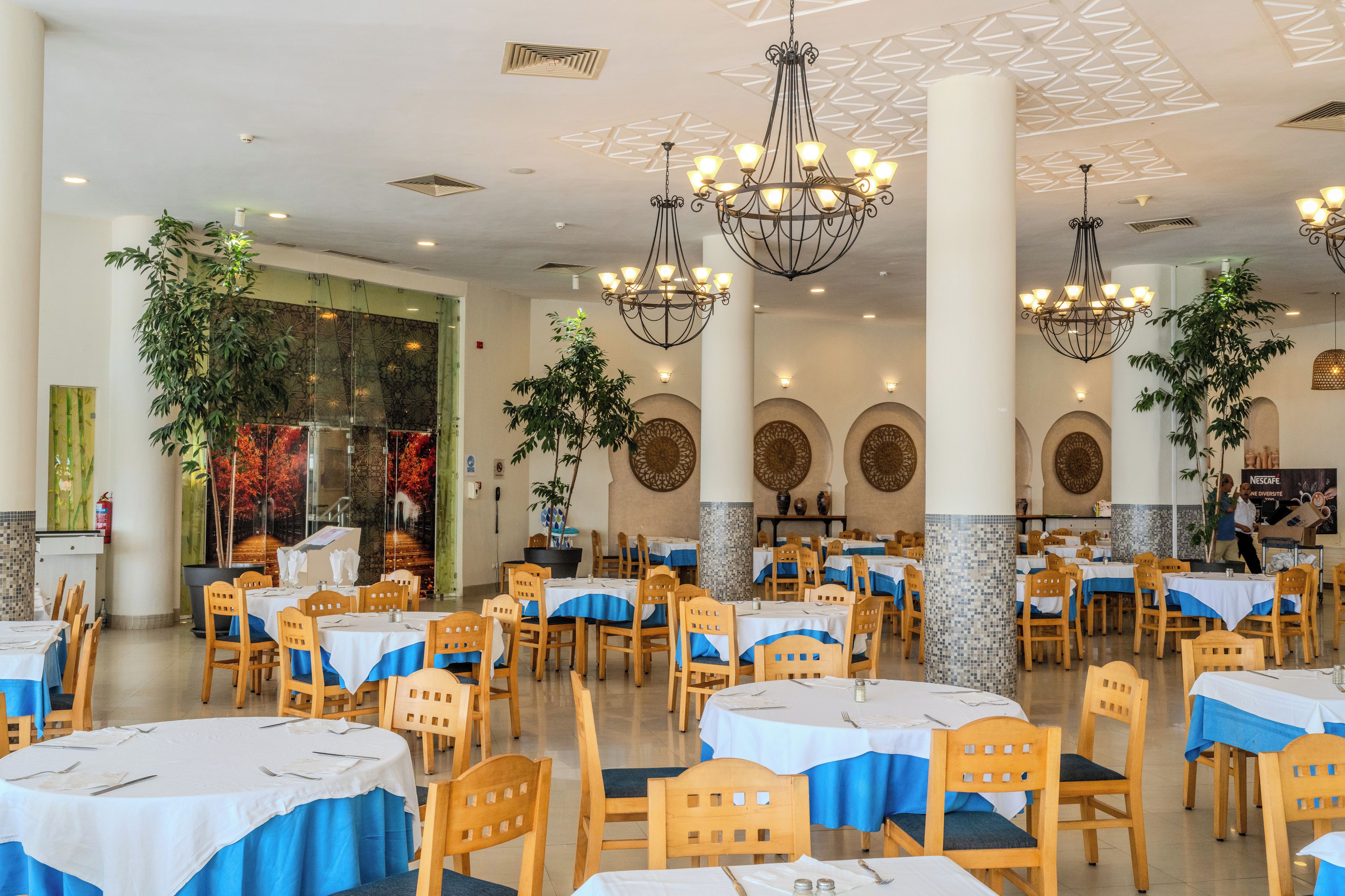 Un vaste espace dédié à la salle à manger, avec de nombreuses tables et chaises, un éclairage décoratif et des plantes en pot.