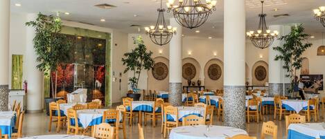 Un vaste espace dédié à la salle à manger, avec de nombreuses tables et chaises, un éclairage décoratif et des plantes en pot.