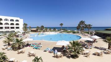 Un resort con una gran piscina rodeada de sillas de descanso y sombrillas, palmeras y vistas al océano.