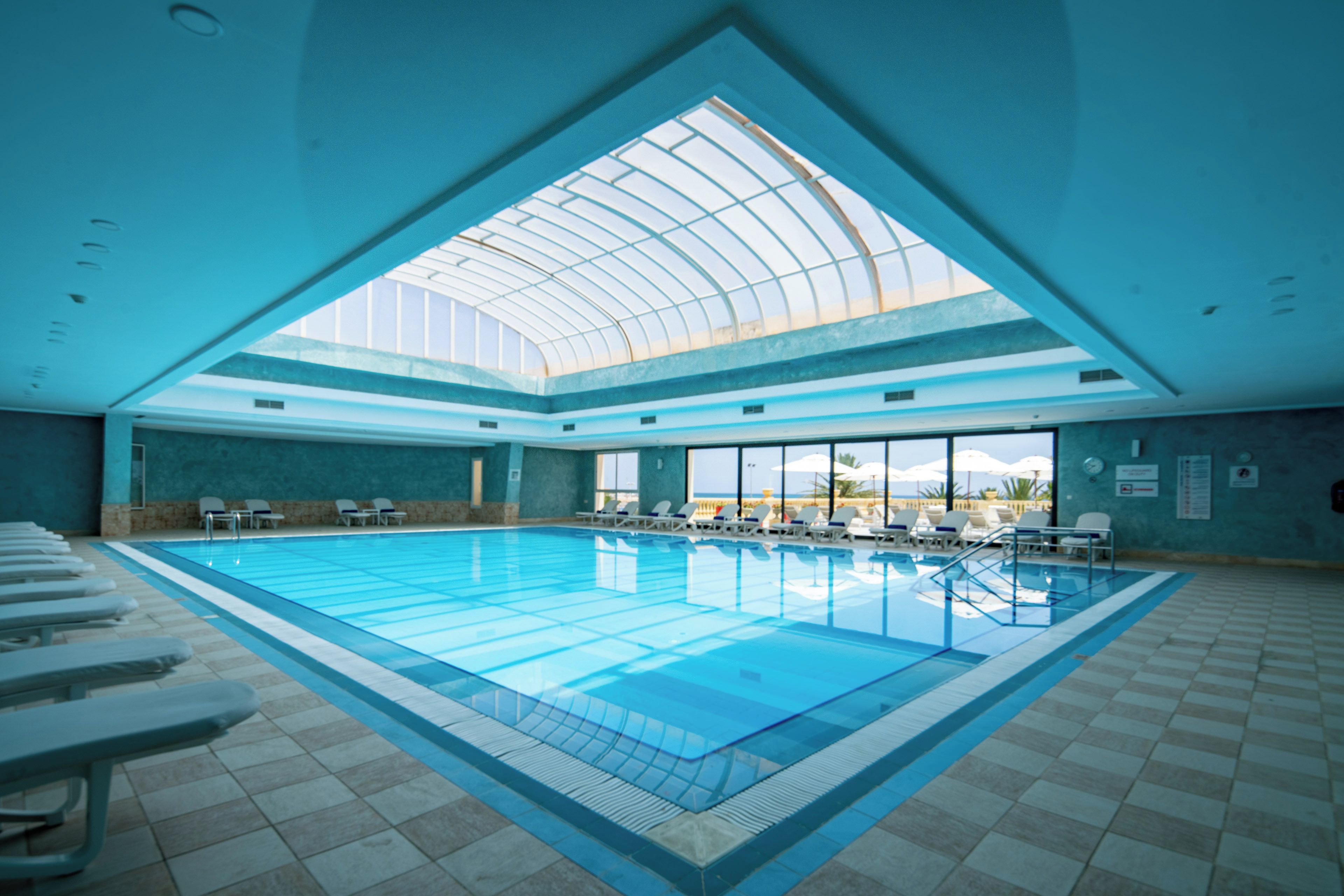 Una piscina interior con techo de vidrio, múltiples carriles y sillones de descanso alrededor del borde.