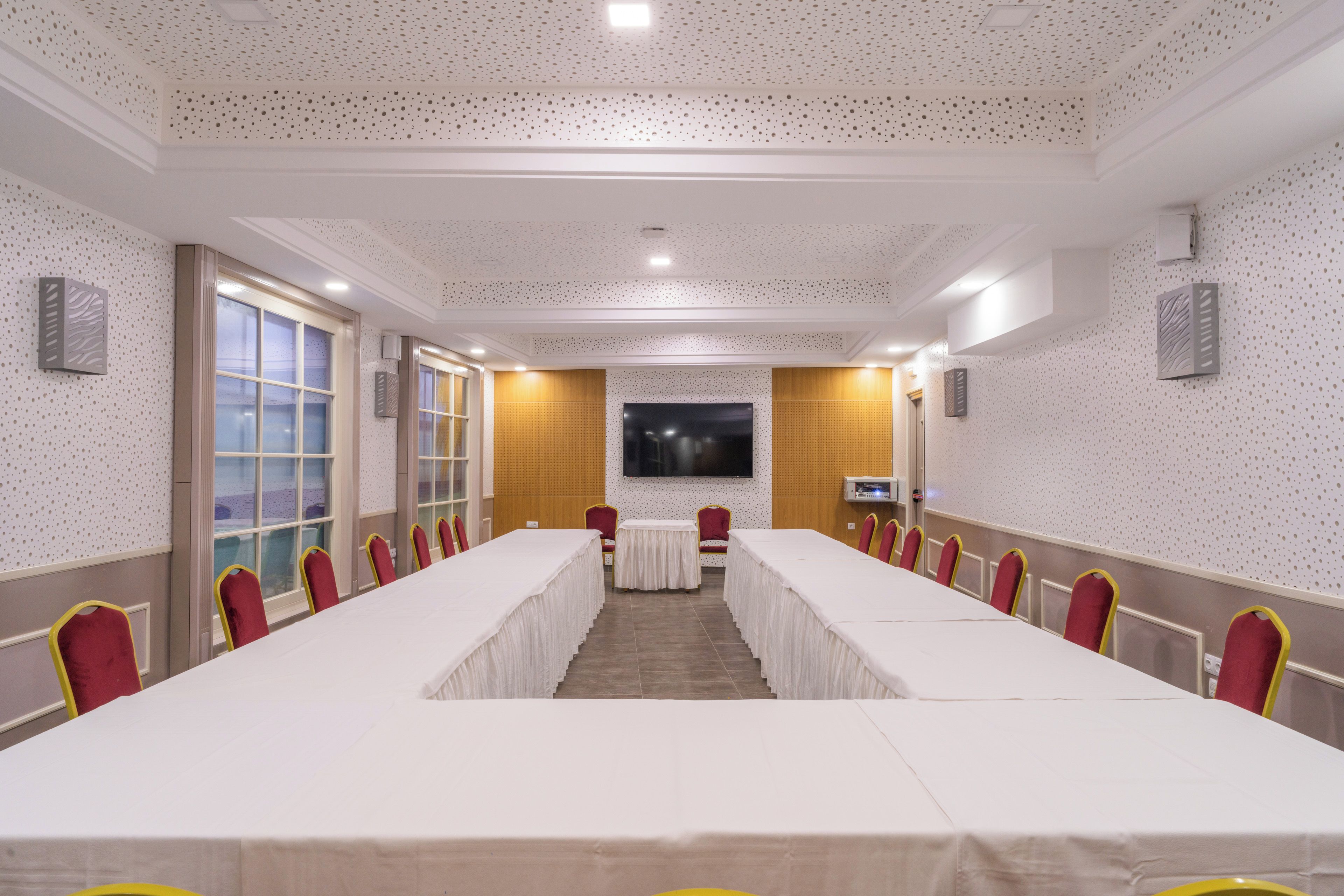 Un salón de conferencias con una larga mesa, sillas rojas y una pantalla grande.