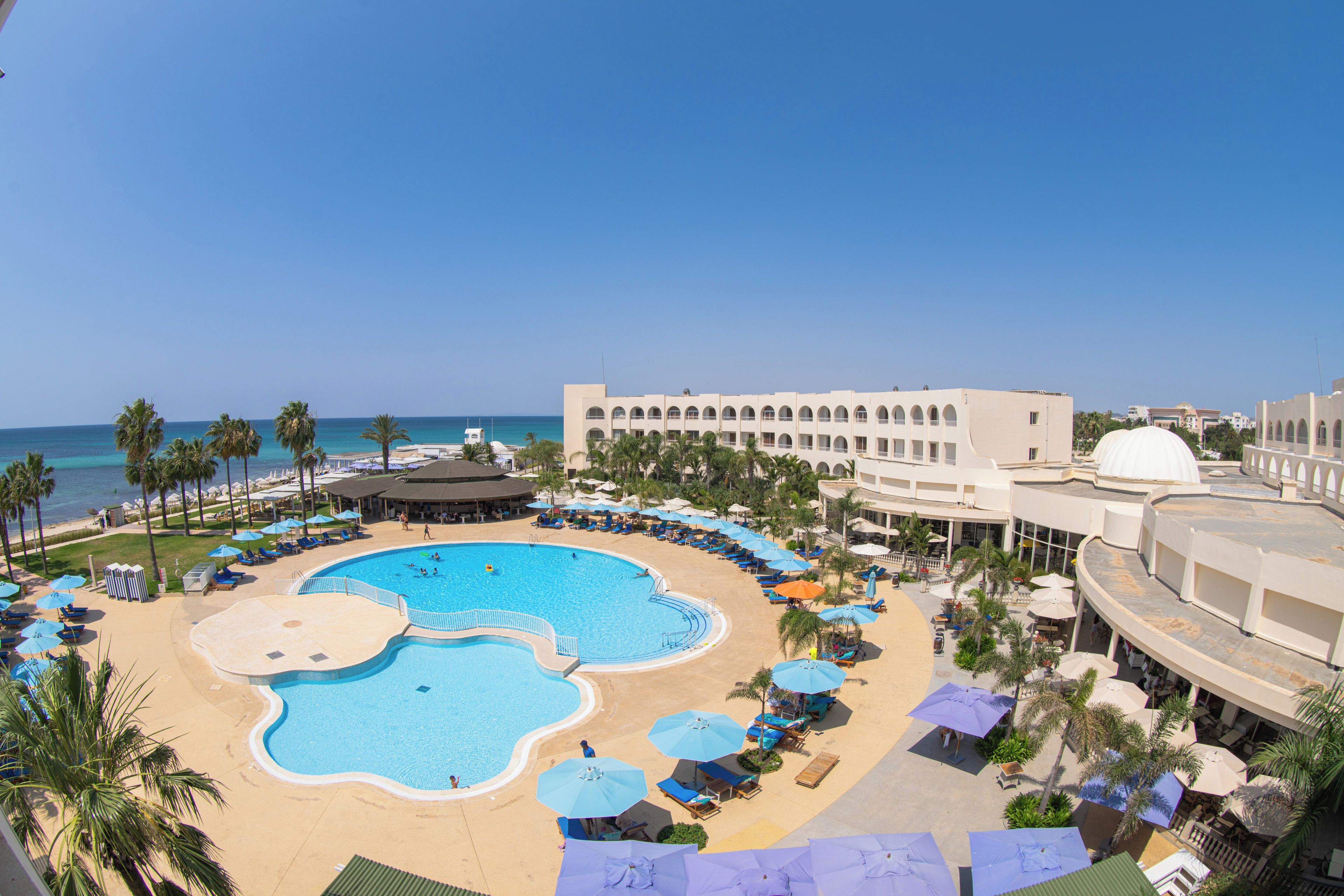 A resort with a central swimming pool, sun loungers, and a view of the ocean.