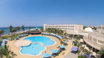 A resort with a central swimming pool, sun loungers, and a view of the ocean.