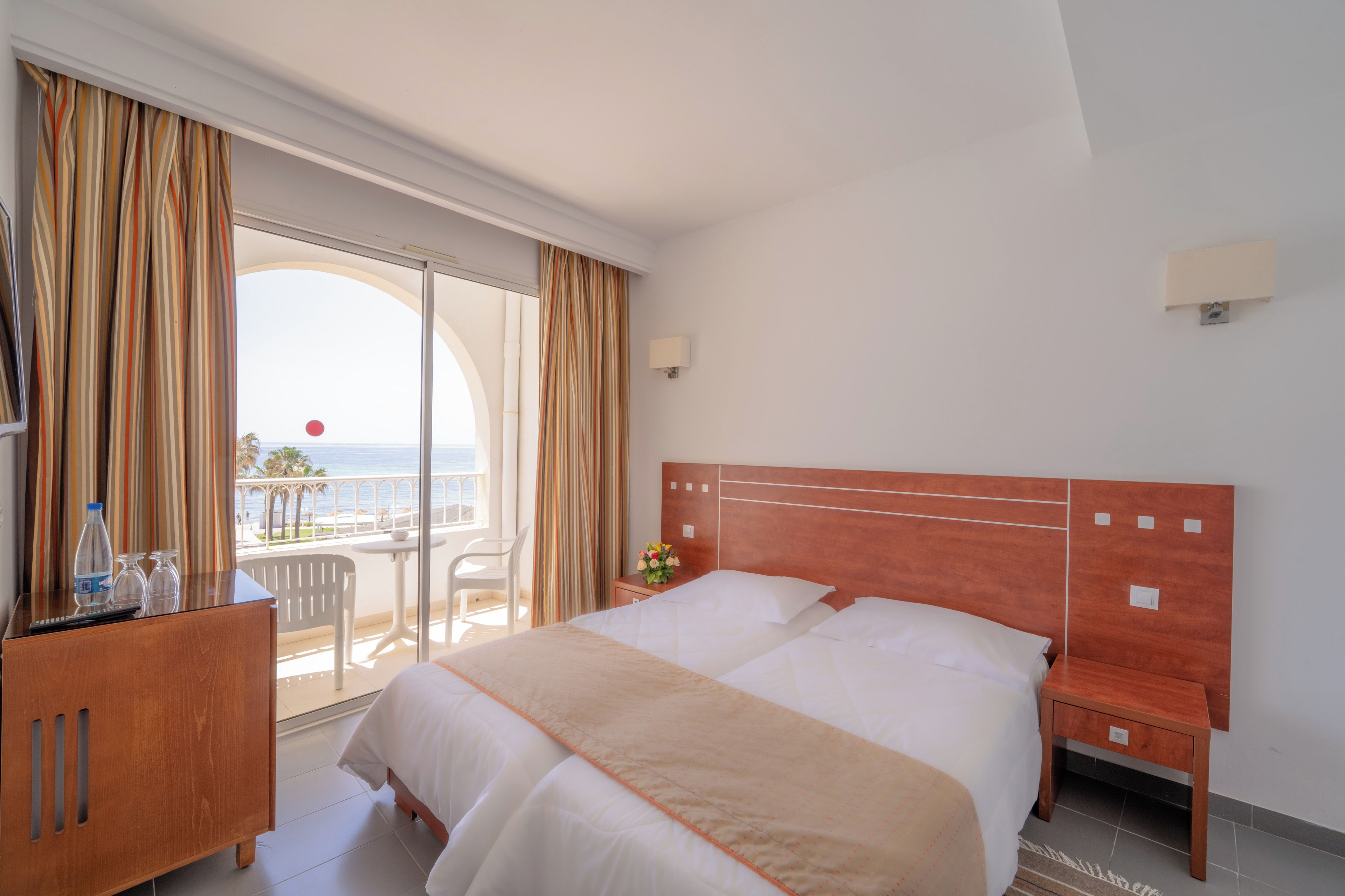 Habitación de hotel con una cama grande, un escritorio con silla, una mesita y vistas al mar desde el balcón.