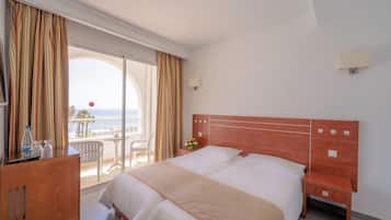 Habitación de hotel con una cama grande, un escritorio con silla, una mesita y vistas al mar desde el balcón.