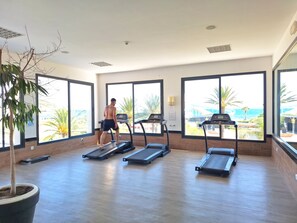 Un gimnasio con cintas de correr y un amplio ventanal con vista a la playa.