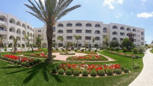 Un hotel de varios pisos con fachada simétrica, ventanas en arco y un patio central con flores rojas y palmeras.