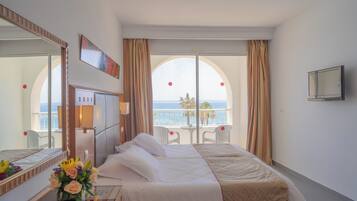 A hotel room with a bed, a desk, a mirror, a TV, and a view of the sea.