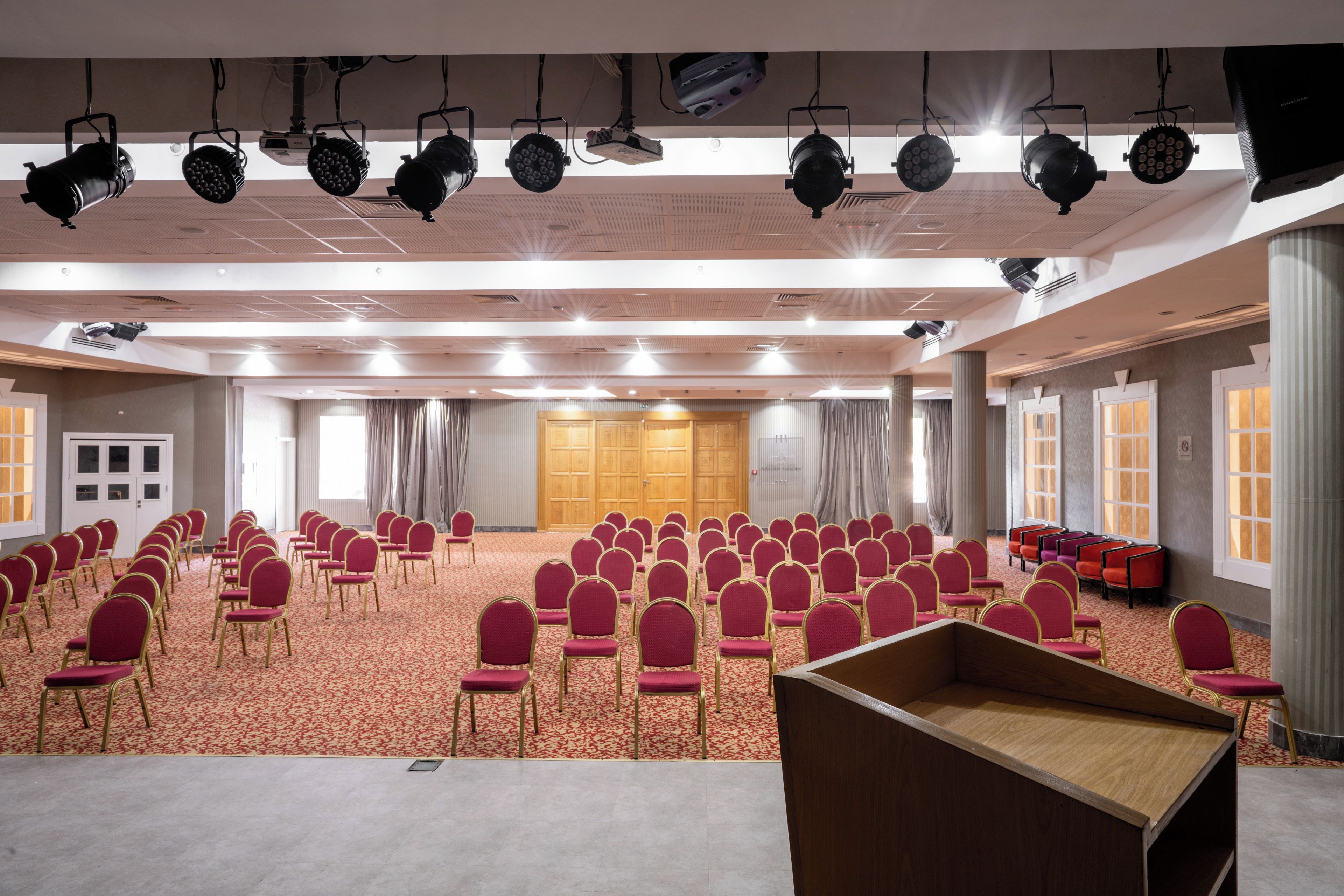 Un salón de conferencias con filas de sillas, un atril e iluminación en el techo.