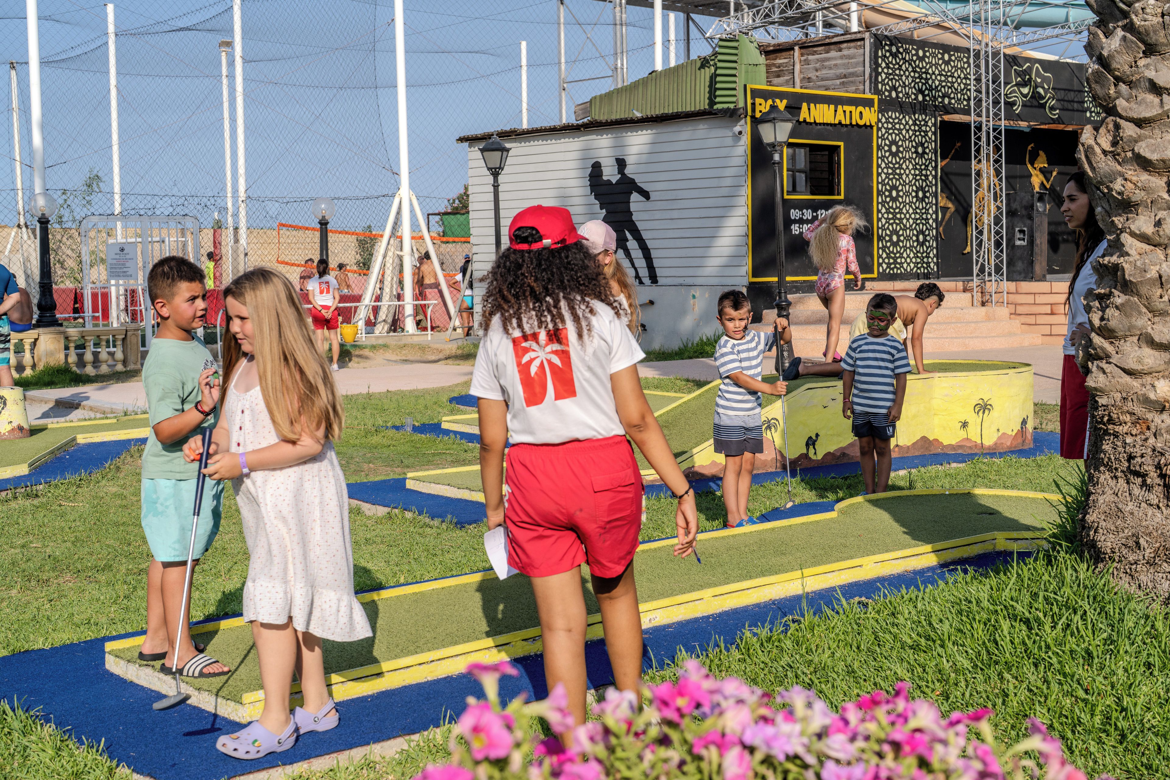 A playground with children playing, surrounded by a fence and a building with a sign.