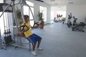 Une salle de sport équipée de machines d’exercice, agrémentée de plantes en pot, où une personne s’entraîne sur une de ces machines.